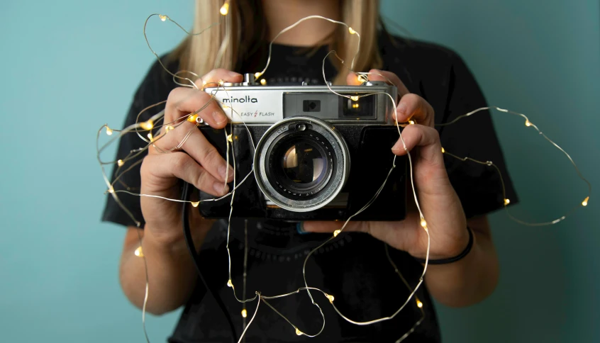 a woman holding a camera in front of her face, inspired by Elsa Bleda, pexels contest winner, string lights, studio medium format photograph, a photo of an old opened camera, minimalistic background