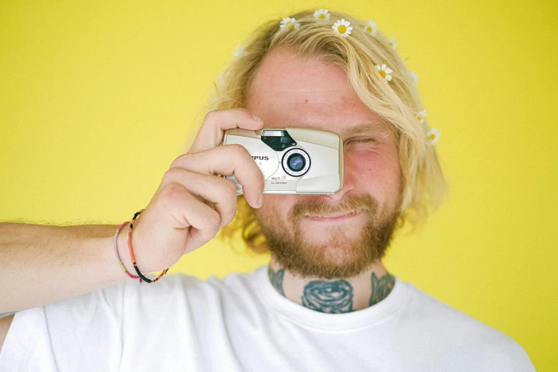 a man taking a picture with a camera, inspired by Cam Sykes, small blond goatee, flower child, disposable colored camera, yellow backdrop