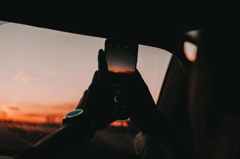 a person taking a picture of a sunset through a car window, trending on pexels, android close to camera, album cover, waist high, rectangle