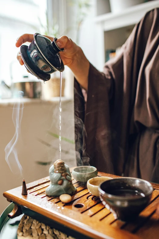 a person pouring tea into a cup on a table, inspired by Tani Bunchō, trending on unsplash, wearing robe, spa, vertical orientation, incense