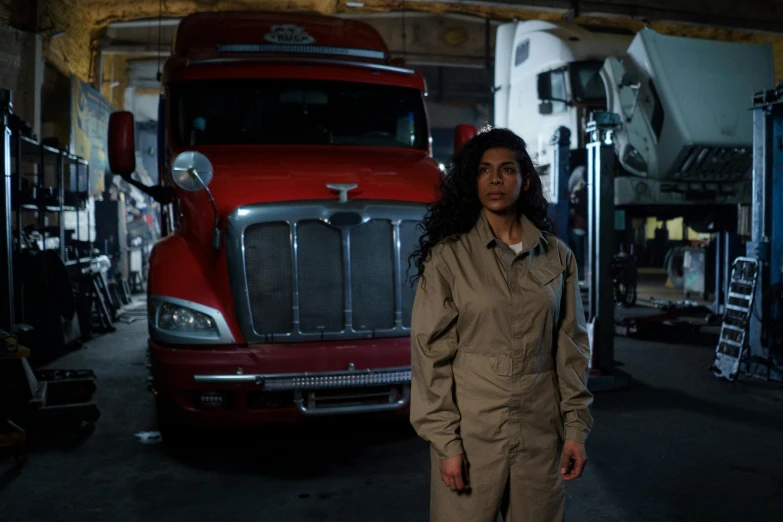 a woman standing in front of a red semi truck, by Dan Frazier, tessa thompson, air force jumpsuit, mechanics, production photo