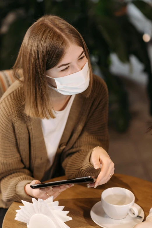 a woman in a face mask sitting at a table with a cat, trending on pexels, happening, android coffee shop, avatar image, surgical mask covering mouth, people sitting at tables