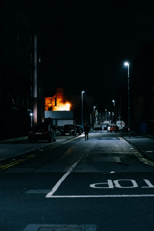 a person walking down a street at night, by Brian Dunlop, burning building, manchester, distant - mid - shot, late morning