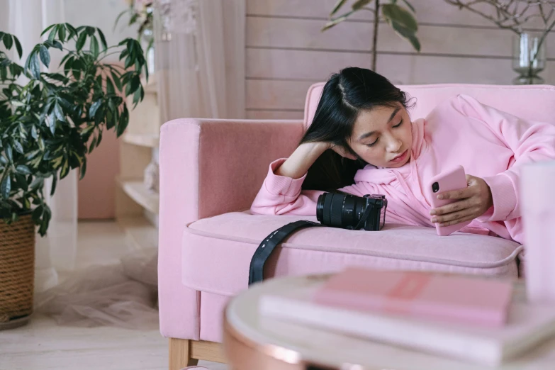 a woman laying on top of a pink couch, a picture, trending on pexels, home album pocket camera photo, trying to study, young asian girl, wearing a tracksuit