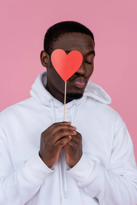 a man in a white hoodie holding a red heart on a stick, trending on pexels, man is with black skin, pink, discord profile picture, studio photo