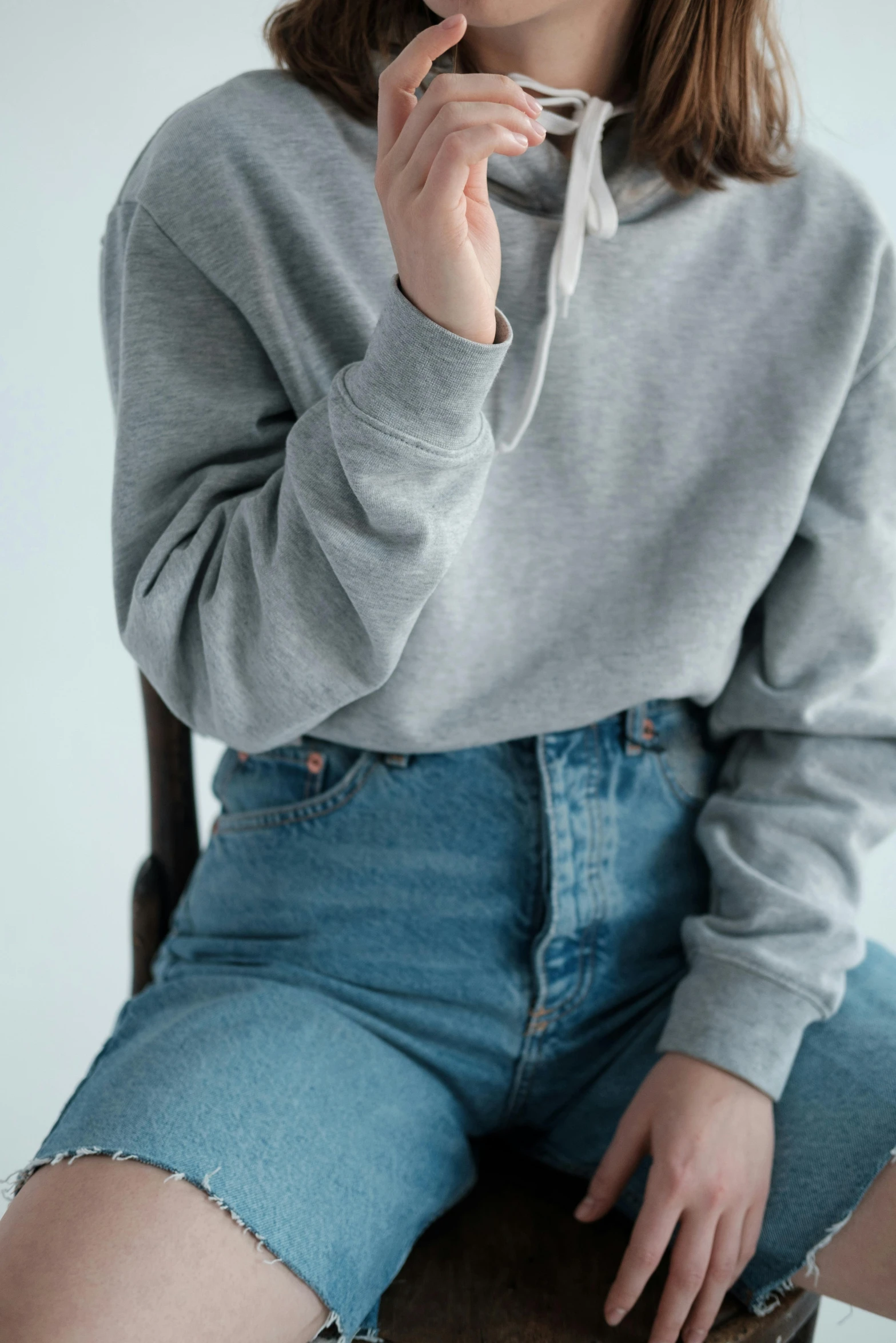 a woman sitting on a chair smoking a cigarette, inspired by Jean Hey, trending on pexels, grey hoodie, denim jeans, round-cropped, pastel clothing