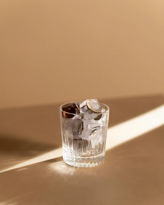 a glass filled with ice sitting on top of a table, an album cover, unsplash, photorealism, muted brown, dappled lighting, product image, small square glasses