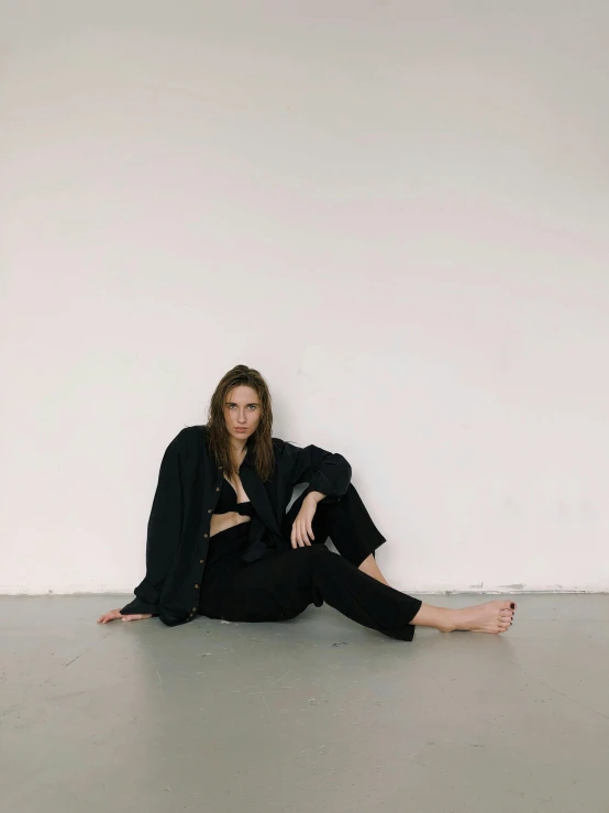 a woman sitting on the floor in a white room, an album cover, by Sara Saftleven, unsplash, visual art, black oversized clothes, gal gadot portrait, baggy black pants, she wears a jacket