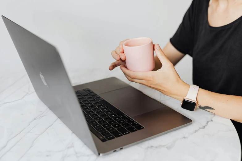 a woman sitting at a table with a laptop and a cup of coffee, by Carey Morris, trending on pexels, pink, holding flask in hand, very minimal, while marble