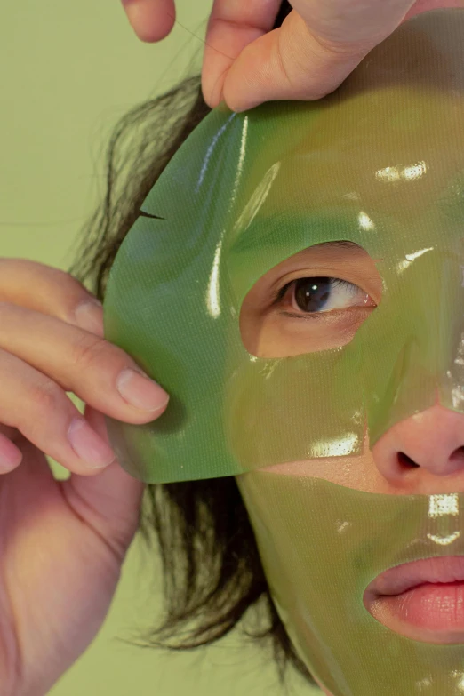 a woman is putting a mask on her face, inspired by Ren Hang, reddit, lush green, in plastic, 3 dimensional, asian