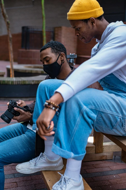 a couple of men sitting on top of a wooden bench, trending on pexels, visual art, holding a camera, wearing mask, black man, denim