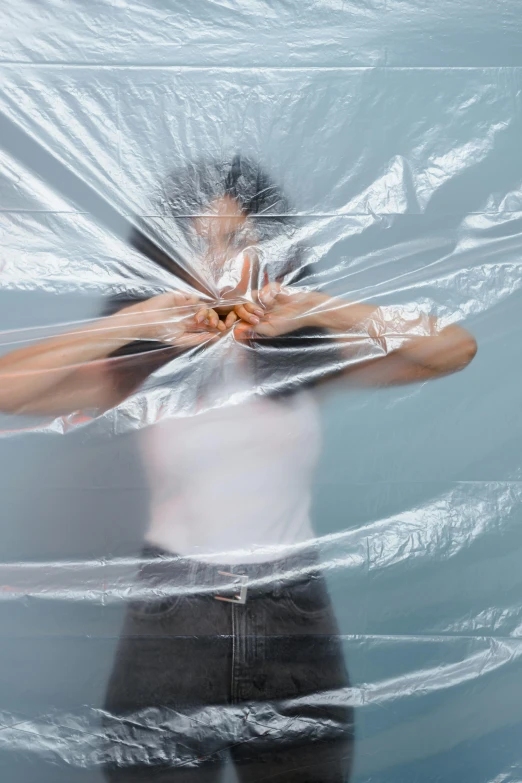 a close up of a person wrapped in plastic, an album cover, inspired by Cornelia Parker, unsplash, plasticien, hands shielding face, silk tarps hanging, asian woman, hdpe