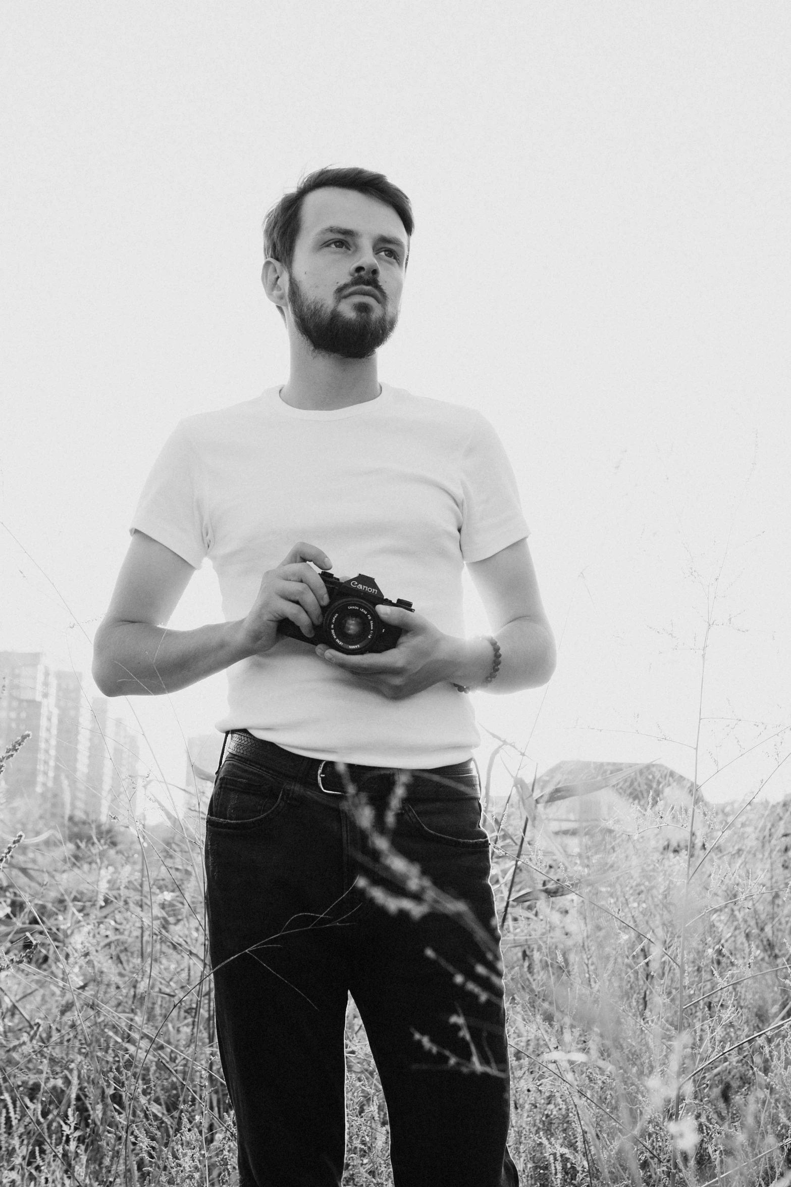 a man standing in a field holding a camera, a black and white photo, inspired by Jean-Yves Couliou, in front of white back drop, liam, zachary corzine, on a pale background