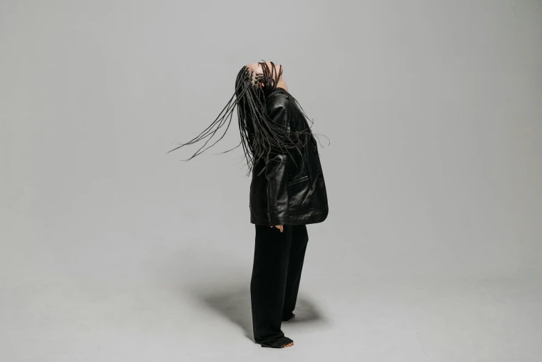 a woman with long hair standing in front of a gray background, an album cover, unsplash, dreadlock black hair, dynamic dancing pose, dressed in black leather, ryoji