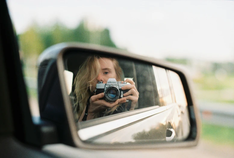 a woman taking a picture of herself in a rear view mirror, unsplash contest winner, photorealism, f 1.4 kodak portra, sydney sweeney, hasselblad medium format camera, holding a camera