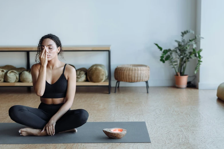 a woman sitting on a yoga mat in a room, trending on pexels, closes her eye, manuka, liquid gold, balance