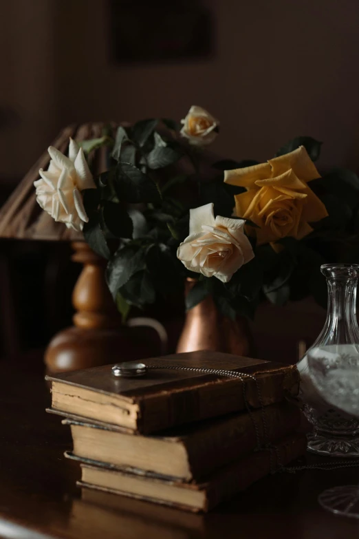 a vase sitting on top of a table next to a stack of books, a still life, pexels, romanticism, yellow rose, in a dark dusty parlor, white roses, victorian photograph