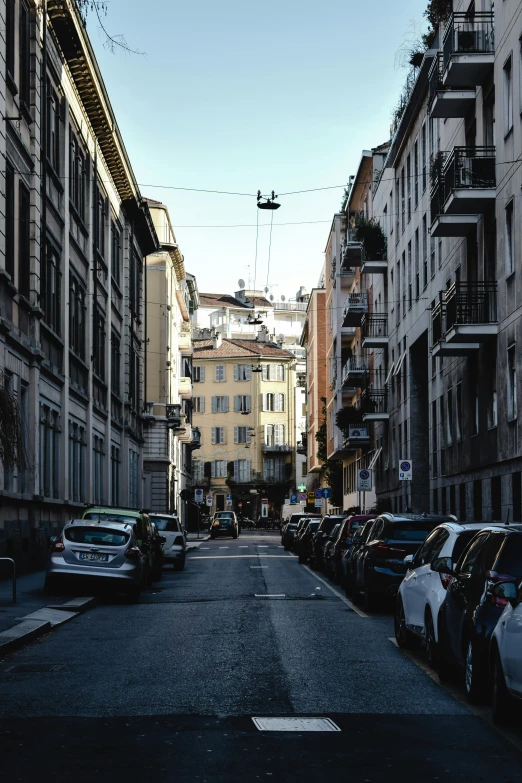 a street lined with parked cars next to tall buildings, a picture, by Alessandro Allori, square, high quality image, quaint, street photograph