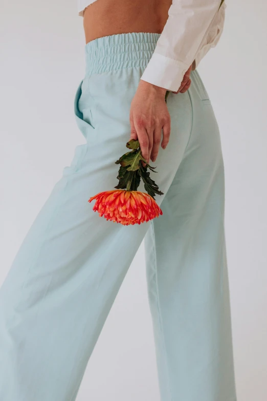 a close up of a person holding a flower, inspired by Jean Hey, aestheticism, blue pants, seafoam green, model posing, carnation