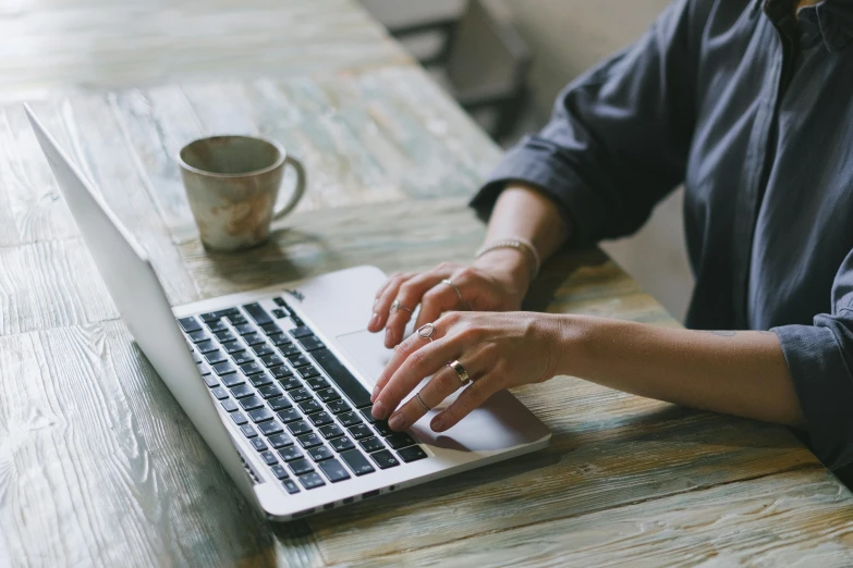 a close up of a person typing on a laptop, by Carey Morris, trending on pexels, table in front with a cup, laura watson, a wooden, background image