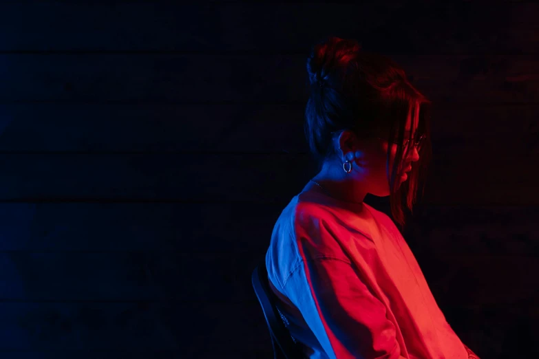 a woman using a laptop computer in a dark room, an album cover, inspired by Elsa Bleda, pexels contest winner, altermodern, red and blue garments, red and blue black light, looking from side, small red lights