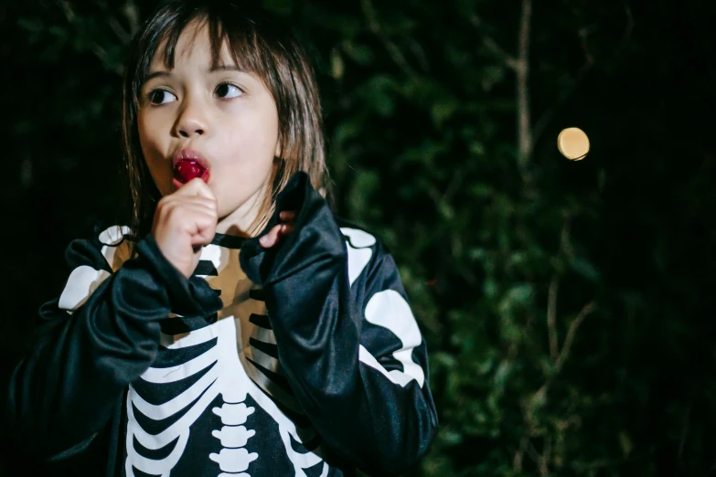 a little girl dressed up in a skeleton costume, a cartoon, by Winona Nelson, pexels, tongue out, night outside, snacks, eleven from stranger things