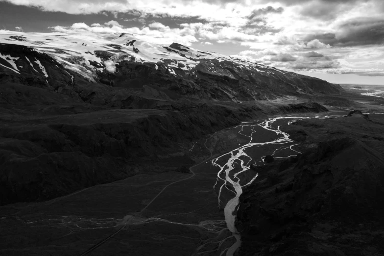 a black and white photo of a river running through a valley, by Jacob Toorenvliet, icelandic valley, drone photograpghy, andes, slight glow