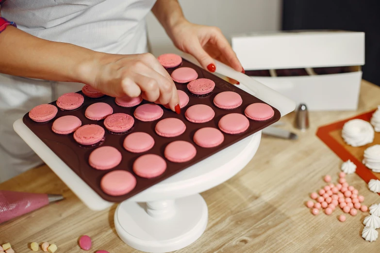 a woman is decorating a cake with pink frosting, a silk screen, trending on pexels, macaron, brown and pink color scheme, buttons, 33mm photo