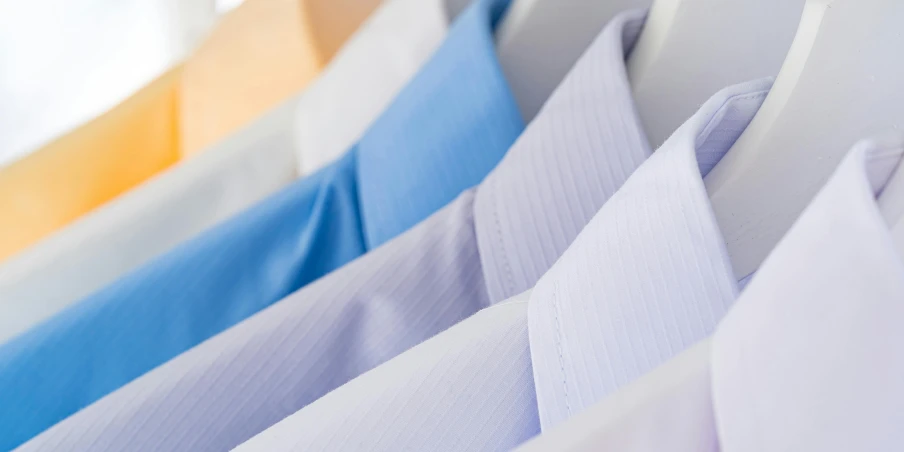 a row of shirts hanging on a rail, sterile colours, neck zoomed in, wearing a light blue suit, full colour