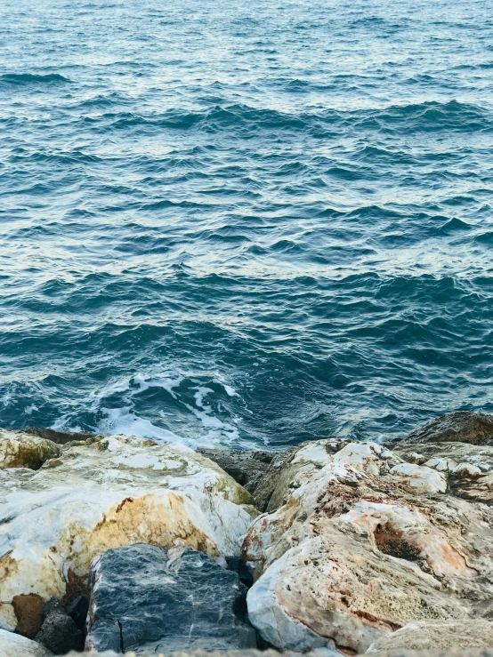 a man sitting on top of a rock next to the ocean, inspired by Winslow Homer, pexels contest winner, romanticism, water ripples, mediterranean, full frame image, today\'s featured photograph 4k