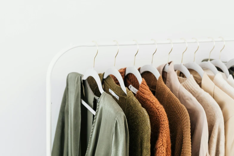 clothes hanging on a rack in front of a white wall, by Nicolette Macnamara, trending on unsplash, green and brown clothes, wearing a fancy jacket, wearing a white sweater, product showcase