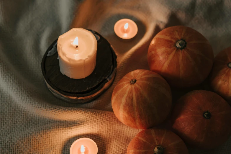 a group of pumpkins sitting next to a lit candle, a still life, trending on pexels, circle, on a velvet table cloth, holding a candle, romantic themed