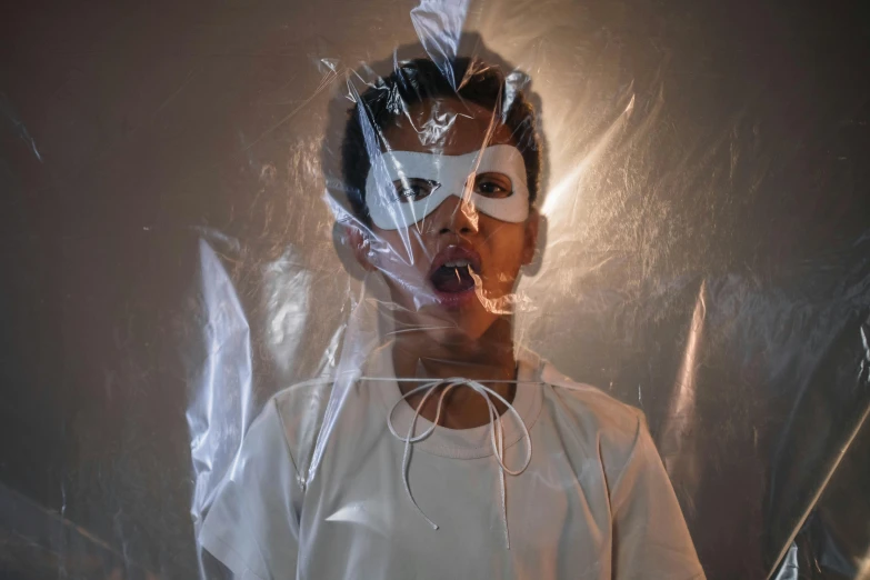 a close up of a person wearing a mask, an album cover, pexels contest winner, conceptual art, wearing translucent sheet, young boy, with wires and bandages, claustrophobic room