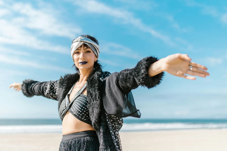 a woman standing on top of a sandy beach, a portrait, by Nina Hamnett, unsplash, hurufiyya, wild rave outfit, waving and smiling, gemma chan, performing a music video