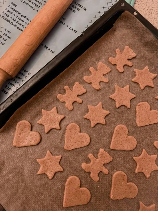 a cookie sheet sitting on top of a table next to a rolling pin, by Julia Pishtar, with stars, cinnamon, thumbnail, hearts
