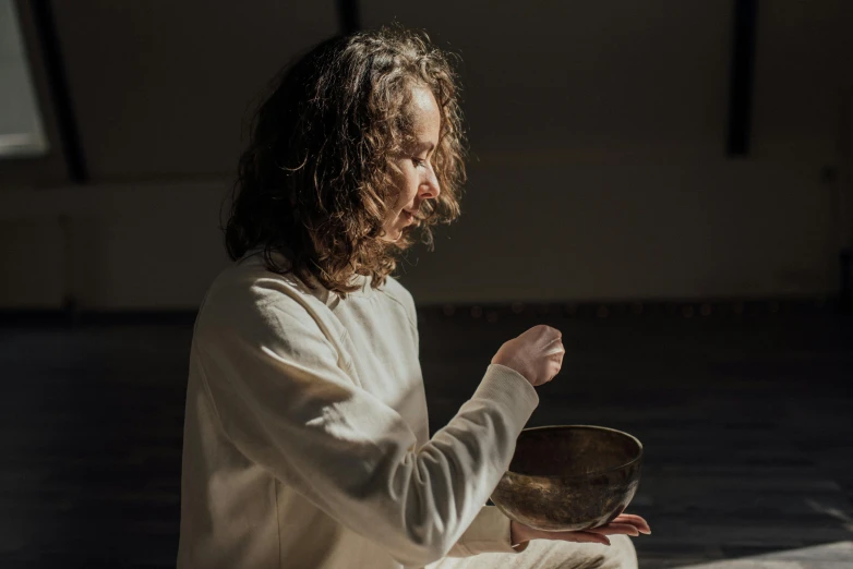 a man sitting on the floor with a bowl in his hand, unsplash, holy ceremony, david shing, press shot, woman