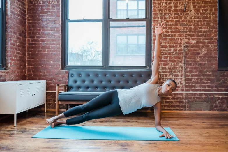 a woman doing a yoga pose on a yoga mat, by Jessie Algie, pexels contest winner, arabesque, zoe saldana, location in a apartment, with abs, kano tan'yu