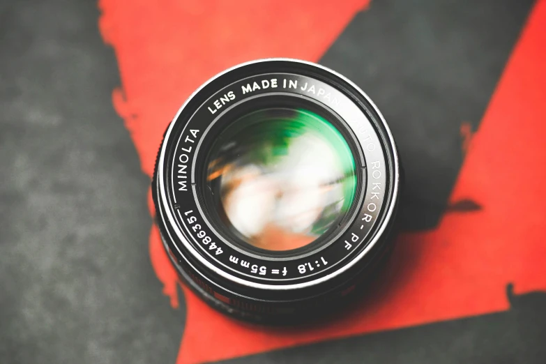 a camera lens sitting on top of a red piece of paper, 50mm f1. 2 noctilux lens, anime style mixed with fujifilm, ecommerce photograph, looking straight into the camera