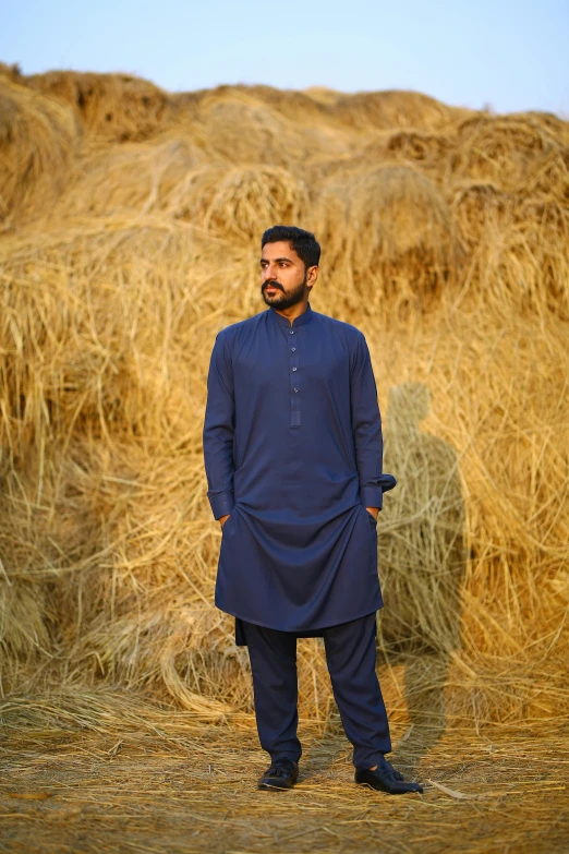 a man standing in front of a pile of hay, an album cover, inspired by Abdullah Gërguri, pexels contest winner, wearing a kurta, navy-blue, modeling shoot, ( ( theatrical ) )