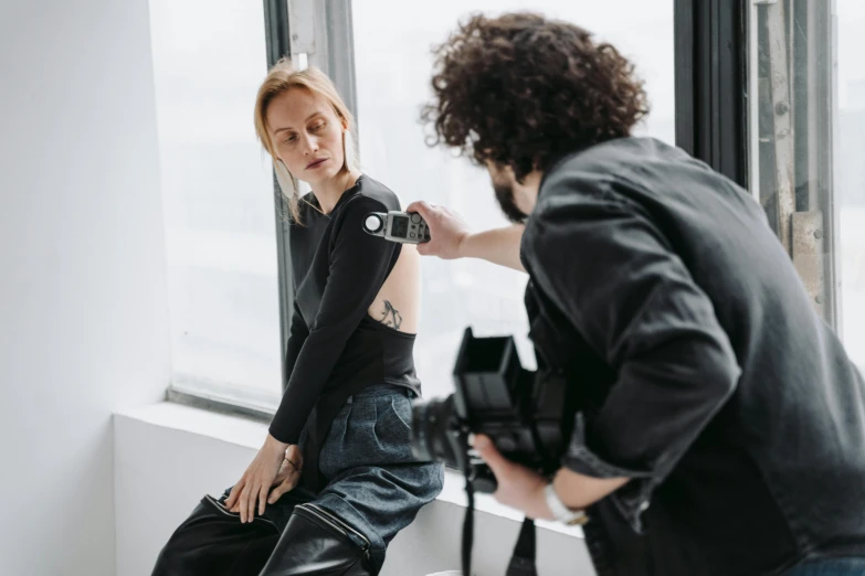 a woman standing next to a man in front of a window, a photo, by Adam Marczyński, trending on pexels, photorealism, wearing jeans, in a photo studio, photoshoot for skincare brand, taking a picture
