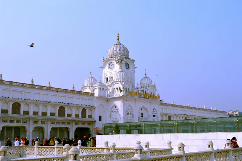 a large white building with a clock tower, by Manjit Bawa, baroque, turban, panoramic, ground - level medium shot, square