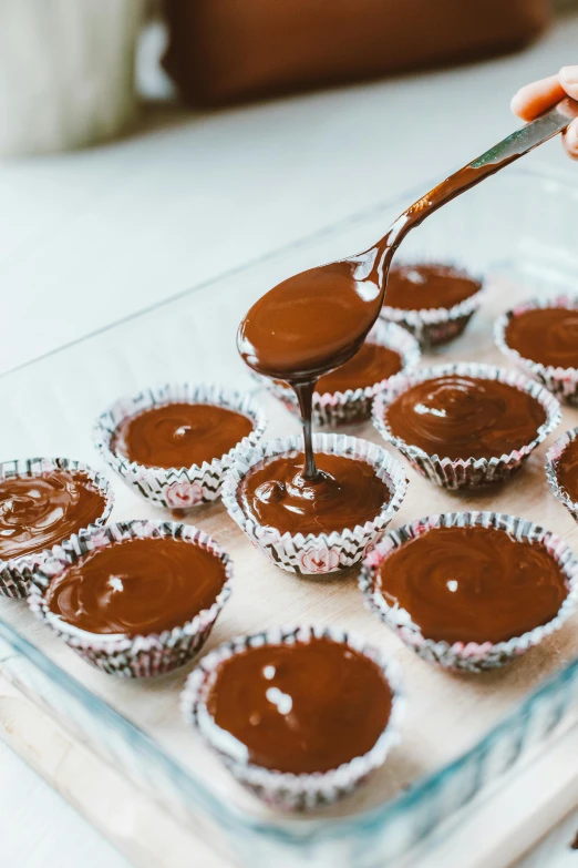 a tray of chocolate cupcakes being drizzled with a spoon, by Lucette Barker, trending on unsplash, kek, caramel, brazilian, brown haired