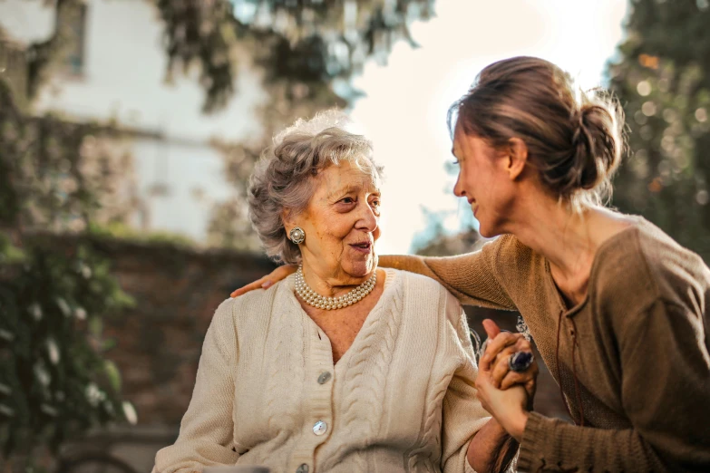 a woman standing next to a woman sitting on a bench, pexels contest winner, old lady screaming and laughing, profile image, nursing, brown