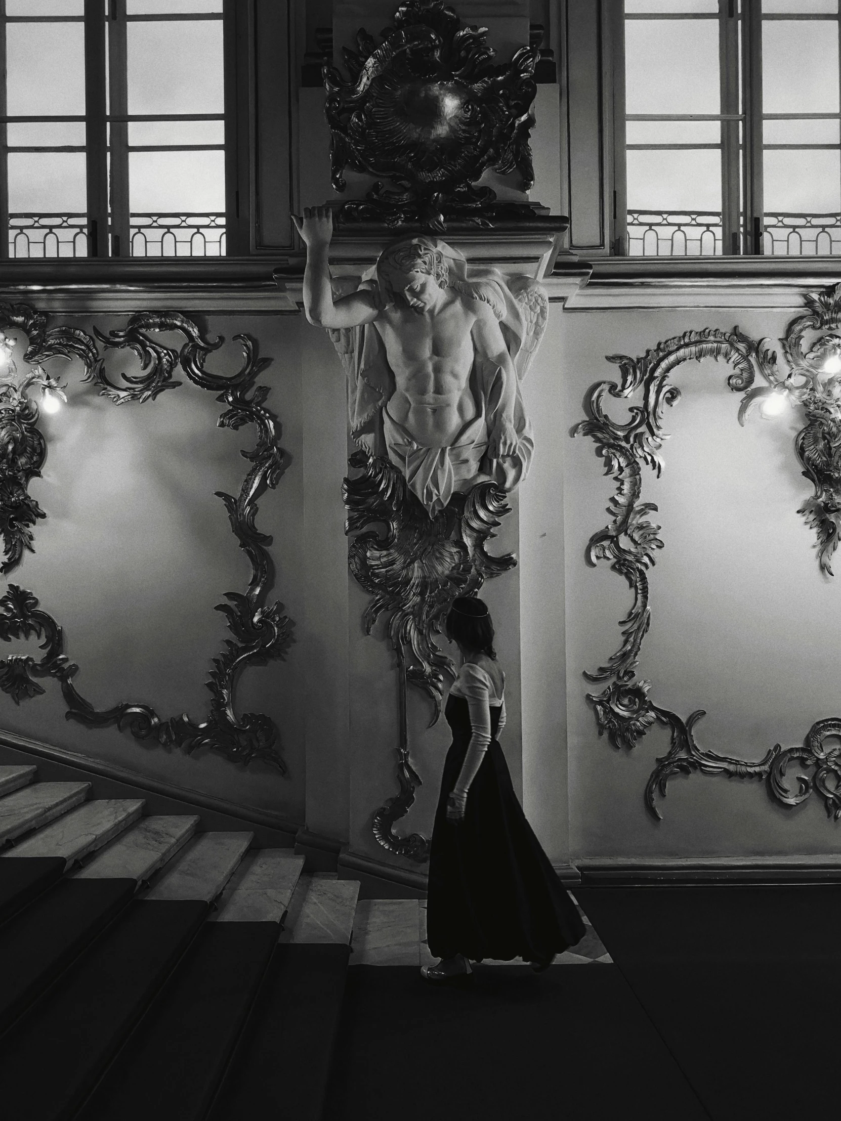 a black and white photo of a woman in a long dress, a black and white photo, inspired by Henryk Siemiradzki, pexels contest winner, baroque, stairway, cherub, rococo decorations, casey baugh and james jean