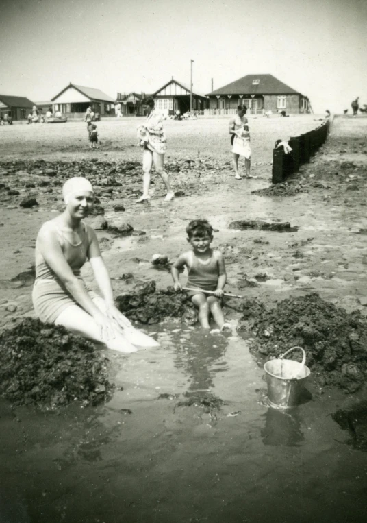 a black and white photo of a woman and a child playing in the sand, wearing a white bathing cap, mud and brick houses, a bald, underwater photograph