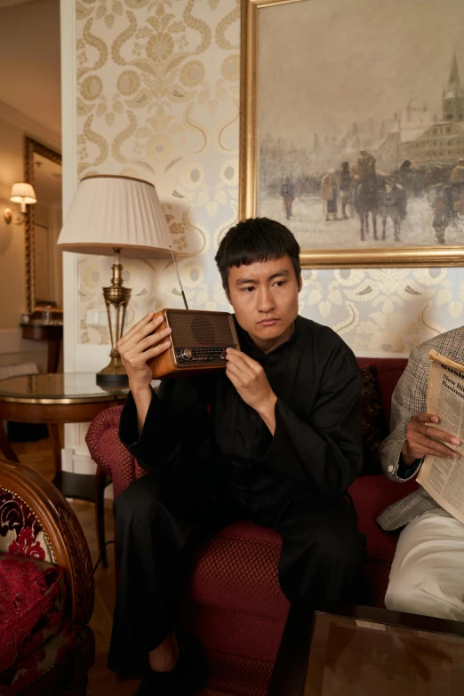 a couple of men sitting on top of a red couch, an album cover, inspired by Fei Danxu, holding spell book, hotel room, taken in the early 2020s, looking at his phone