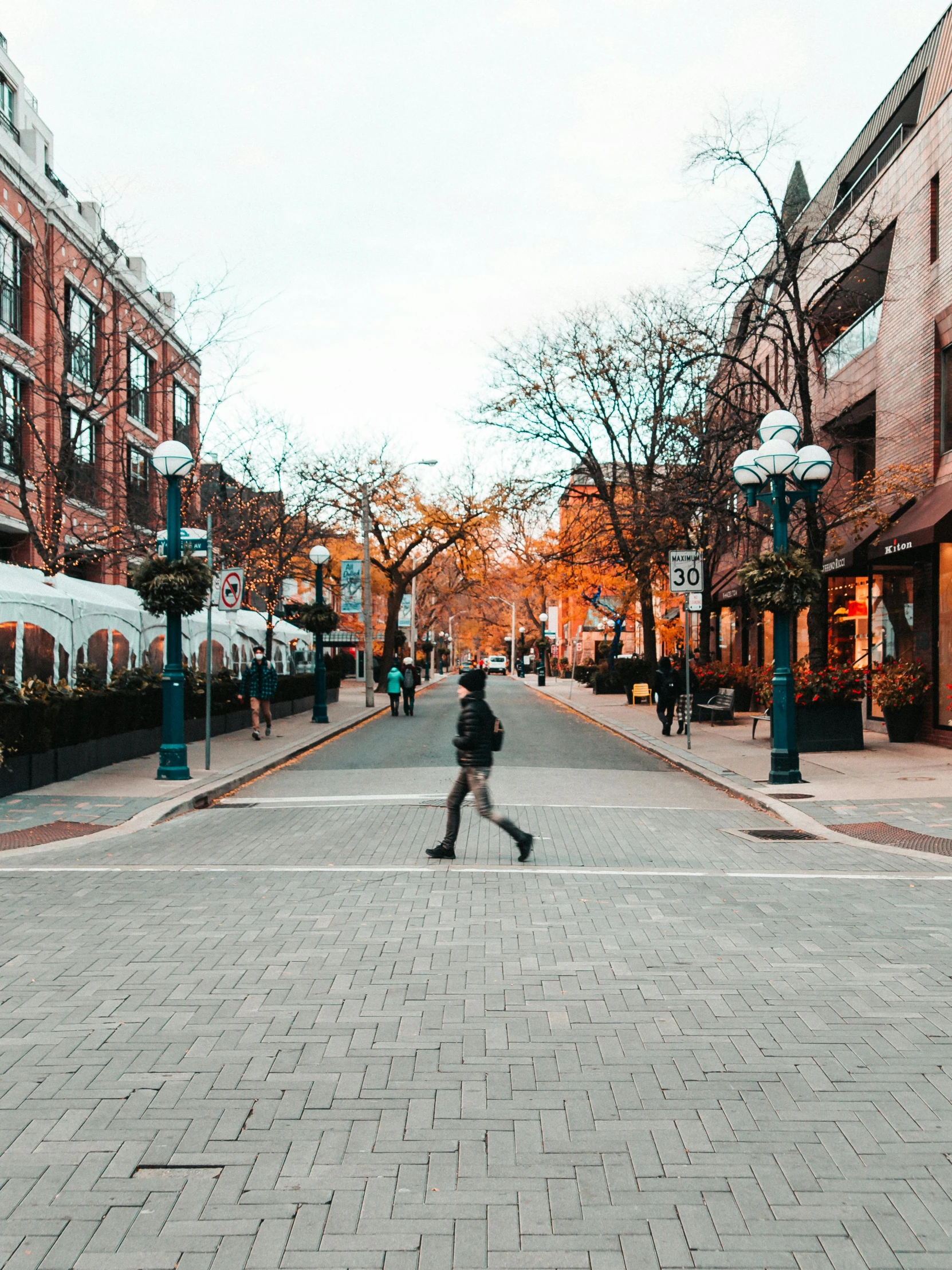 a person riding a skateboard down a city street, pexels contest winner, colonial era street, on a sidewalk of vancouver, streetlamps with orange light, whistler