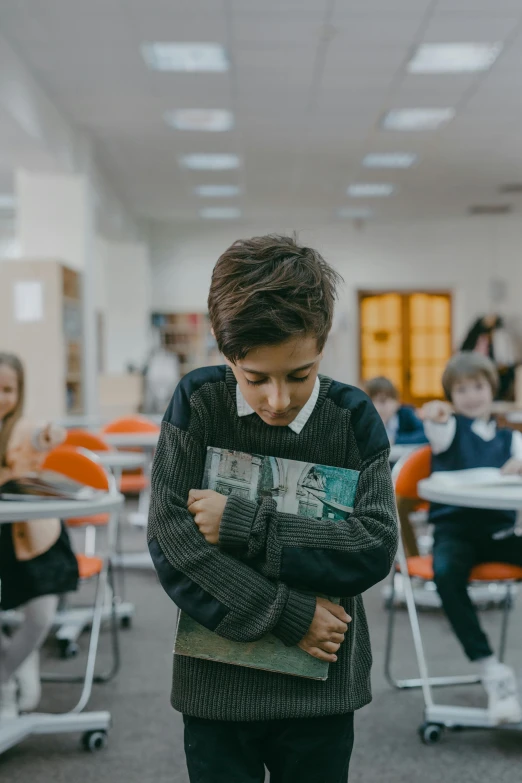 a boy standing in a classroom holding a book, an album cover, by Adam Marczyński, pexels contest winner, with a hurt expression, gif, panoramic view of girl, bullying