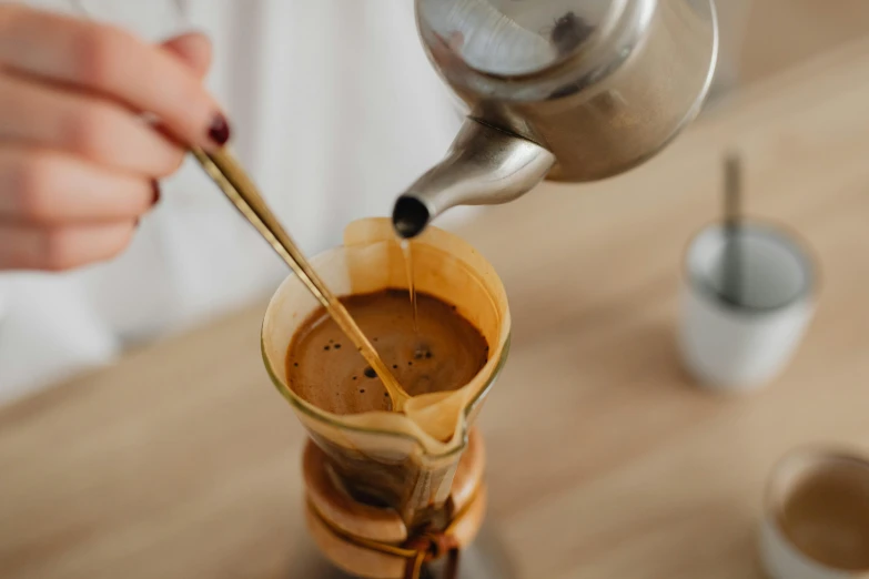 a close up of a person pouring a cup of coffee, by Julia Pishtar, straining, cone shaped, gold, high quality product image”