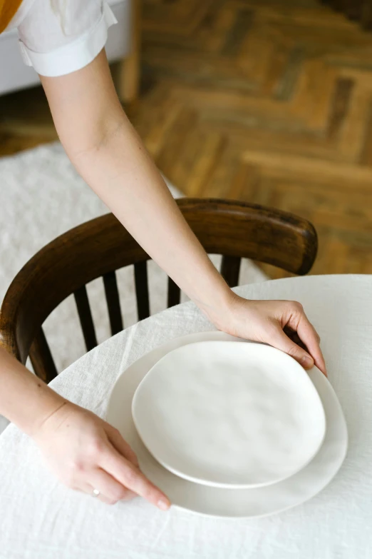 a woman is setting a white plate on a table, by Maeda Seison, soft skin, 4l, designer product, 16k